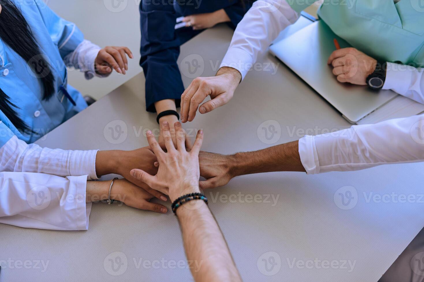 A group of doctors and a medical nurse join their hands together on a table, showcasing the unwavering teamwork and solidarity that drives their collective efforts in the healthcare field photo