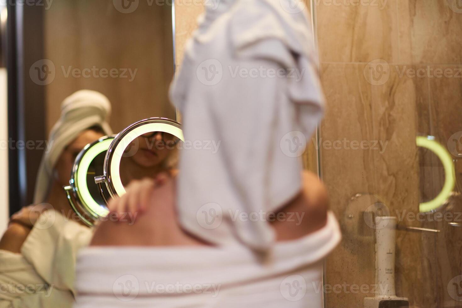 A woman gracefully applies nourishing moisturizer to her shoulder after a relaxing bath, embodying a radiant and rejuvenated skincare routine photo