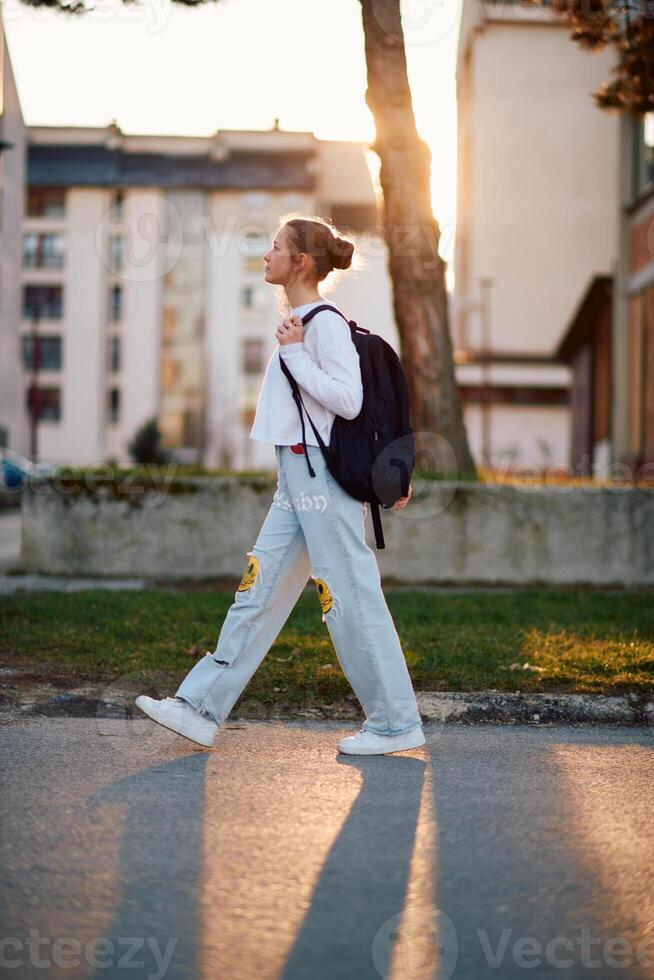 A beautiful European teenager, captured in a side-profile portrait, walks home during sunset after school, carrying her backpack photo