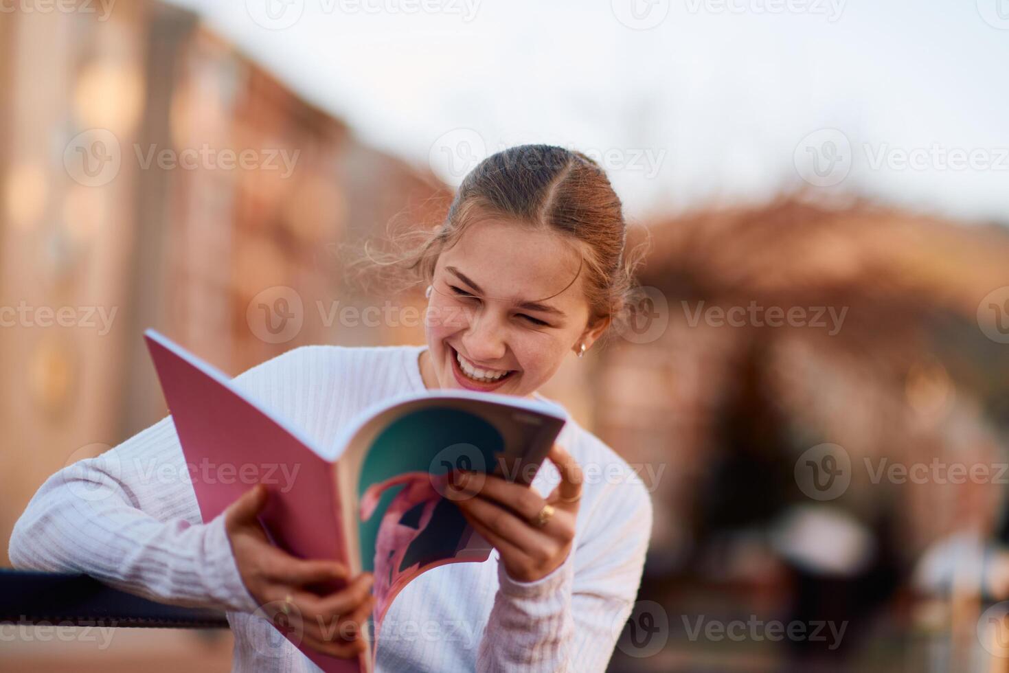 A beautiful blonde teenager sits on a bench in the park, taking a break from school to immerse herself in a book, accompanied by her school backpack photo