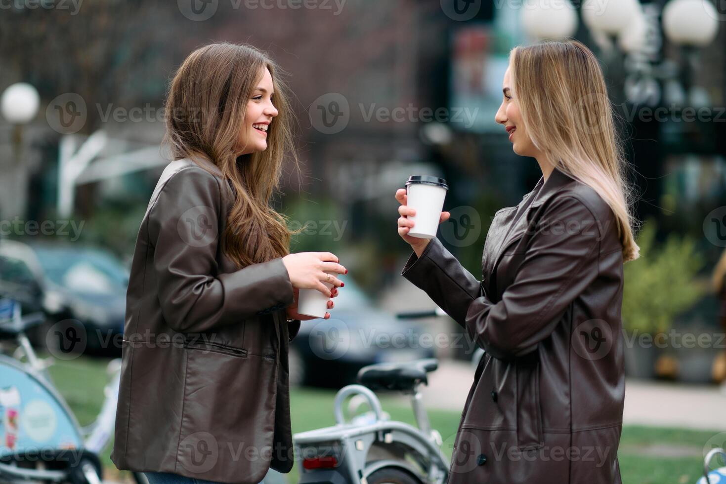 Two businesswomen take a break outside their company, enjoying a moment of relaxation as they hold cups of coffee in their hands photo