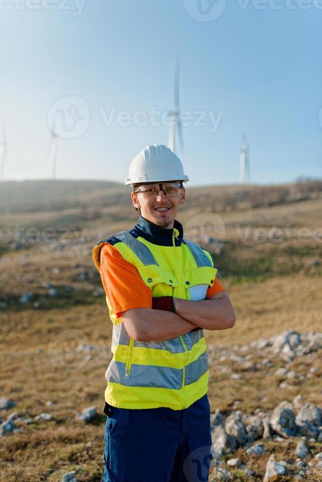 A young engineer with crossed arms inspects a field of wind turbines, displaying confidence and dedication to renewable energy projects. photo