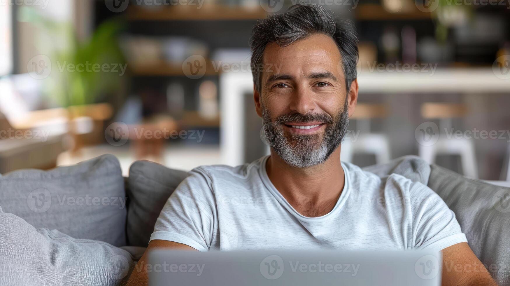 A man smiles as he works on a laptop while sitting on a couch photo