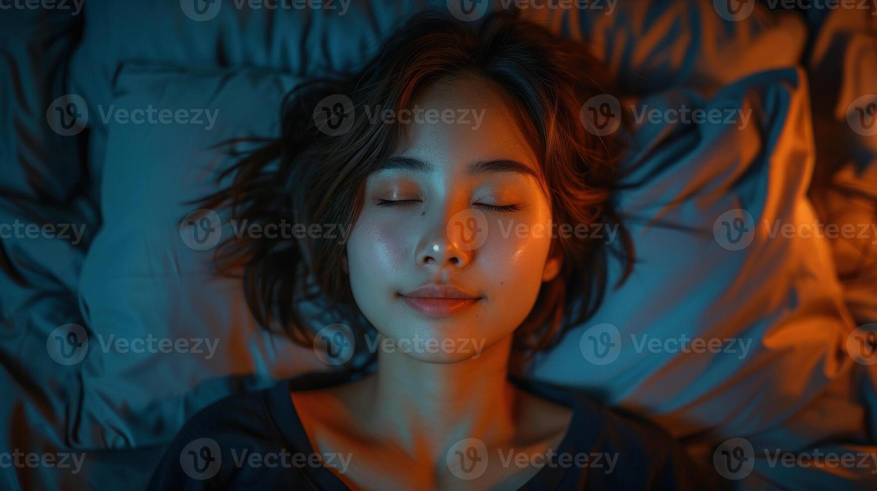 A woman in bed with eyes closed, warm orange light on face, cool blue light elsewhere photo