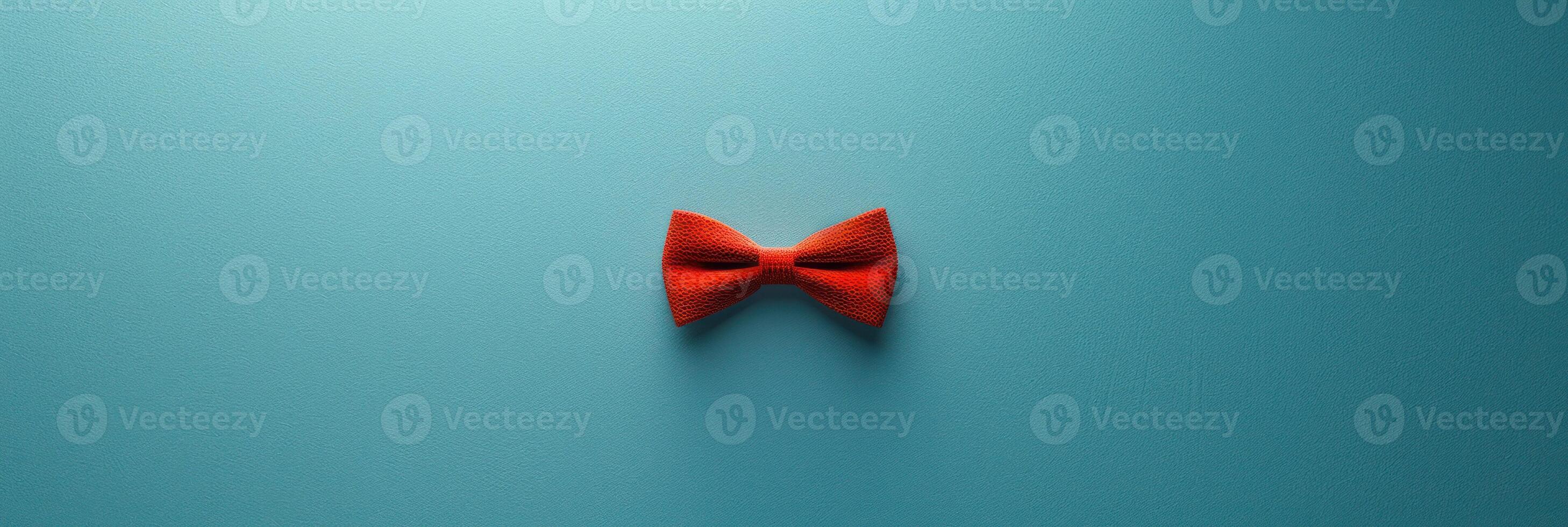 A single red bowtie sits on a teal background, creating a minimalist and stylish image photo