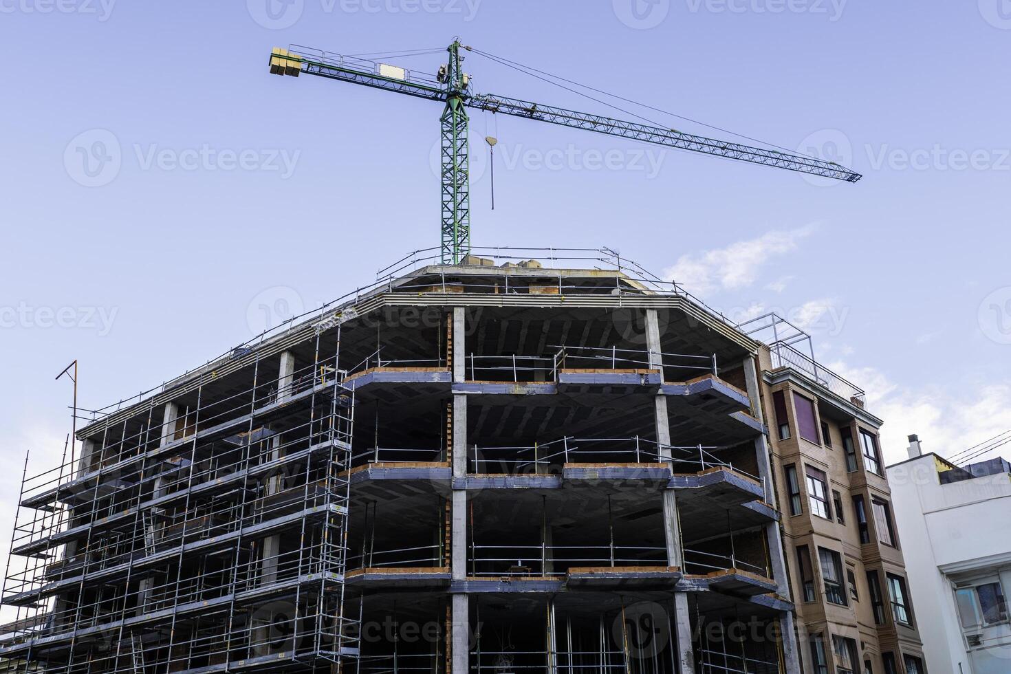 View of a construction site featuring a green crane and the framework of a multi-story building under construction photo