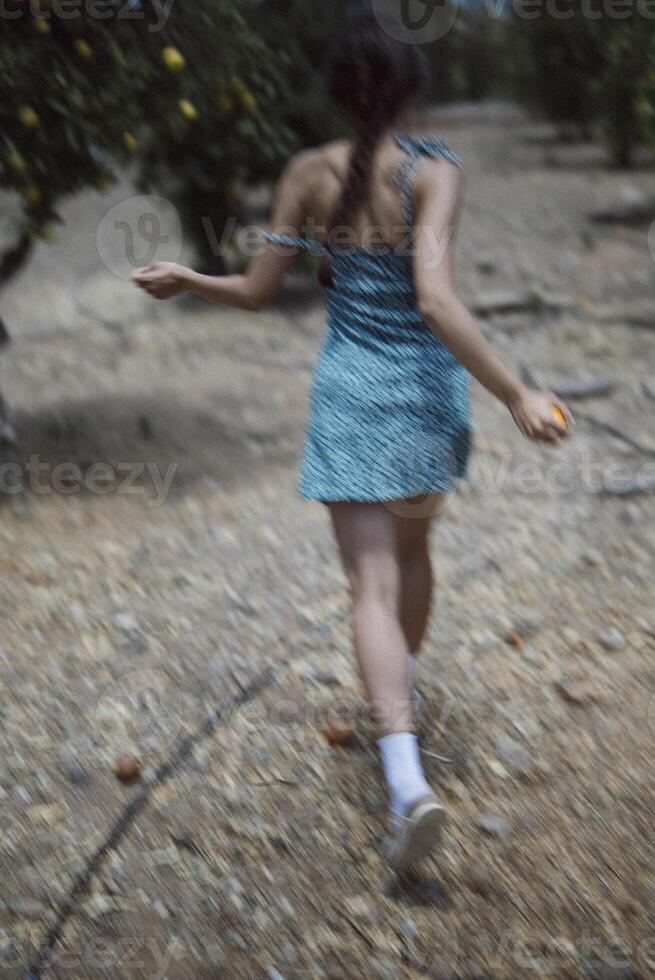 A woman in a summer dress walks in an orchard, holding fruits among green trees and fresh fruits photo