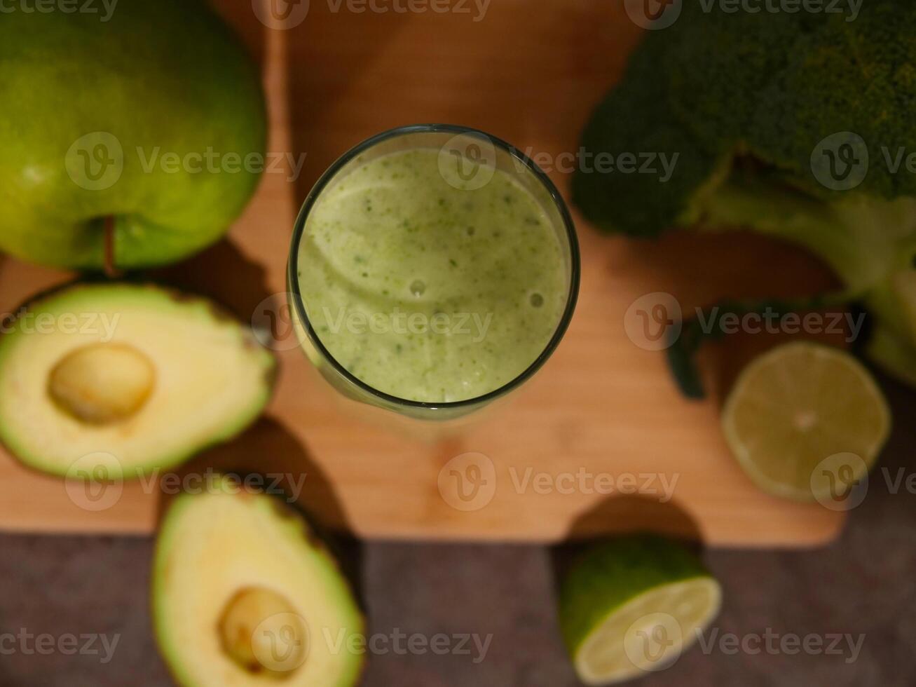 Green smoothie in glass surrounded by avocado, lime, broccoli, apple, cucumber. Perfect smoothie for health, detox, and nutrition content. fresh ingredients and benefits of this vibrant smoothie. photo