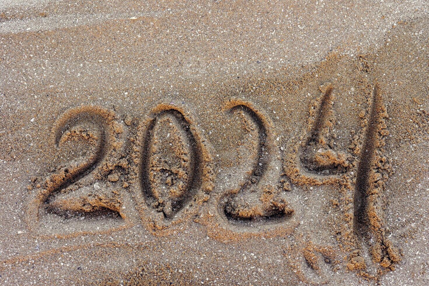 Happy New Year 2024, lettering message handwritten on the beach Numbers 2024 year sand background. photo