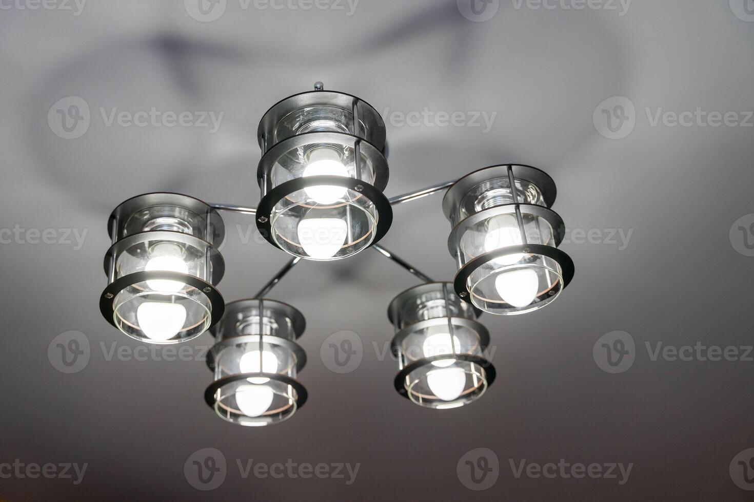 A modern black metal chandelier with five glass shades hangs from a ceiling photo