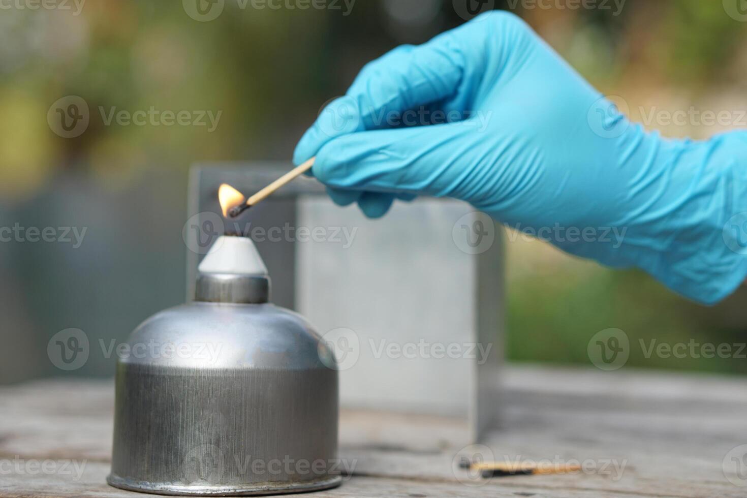 Close up hand wears blue glove, hold a burning match to light fire on alcohol lantern or laboratory lamp. Concept, equipment or tool for science experiment. photo