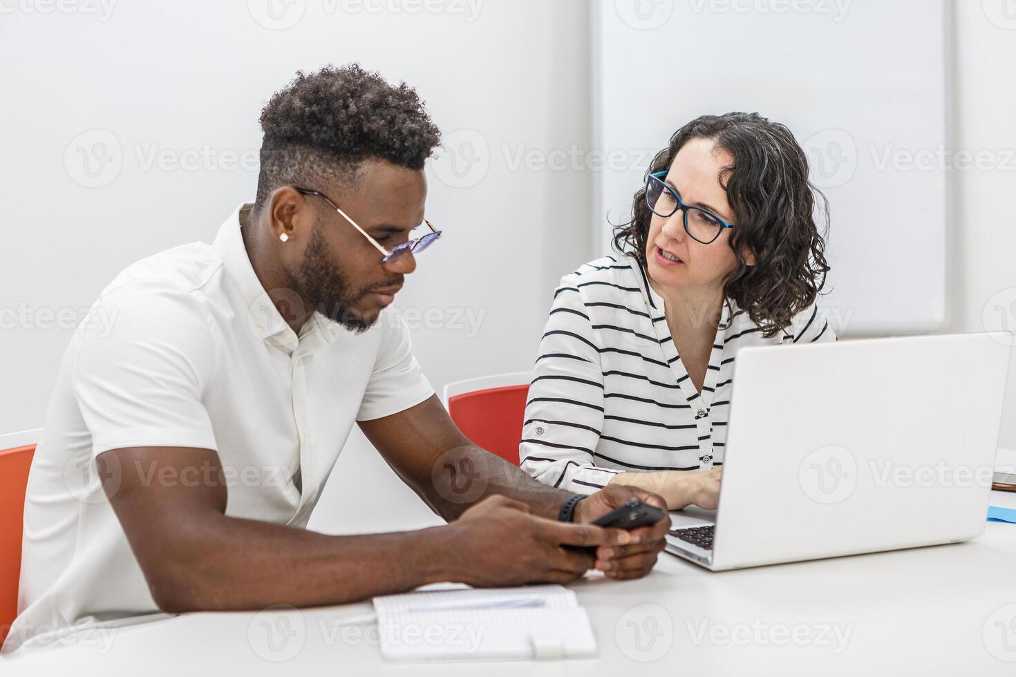 Man and Woman Collaborating on Project in Office Using Laptop and Smartphone photo