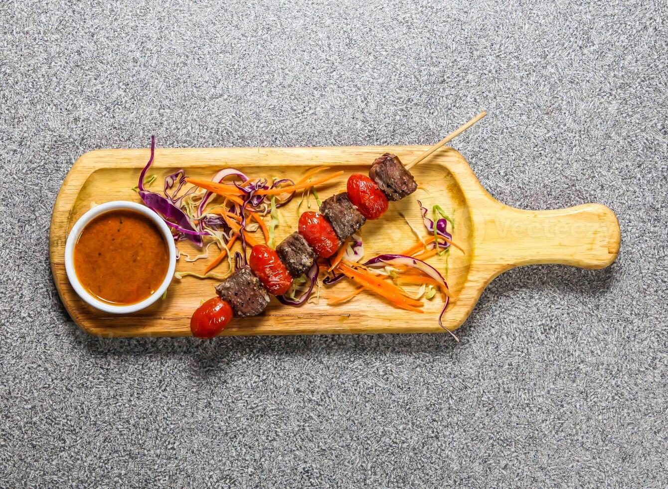 beef fillet satay skewers with chilli sauce served on wooden bard isolated on grey background top view of hong kong fastfood photo