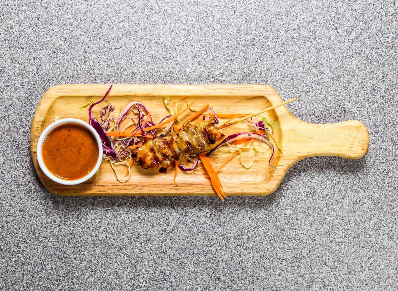 Chicken bbq satay with chilli sauce served on wooden bard isolated on grey background top view of hong kong fastfood photo
