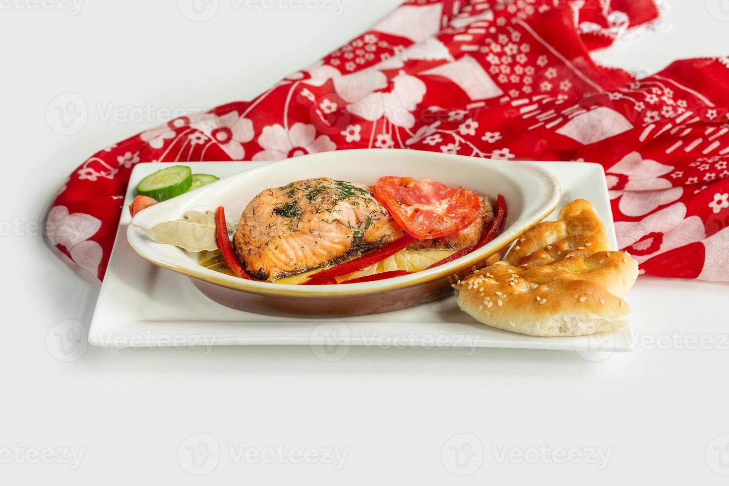 Baked salmon fillet with pita bread, cucumber, tomato in a dish isolated on colorful table cloth top view on grey background photo
