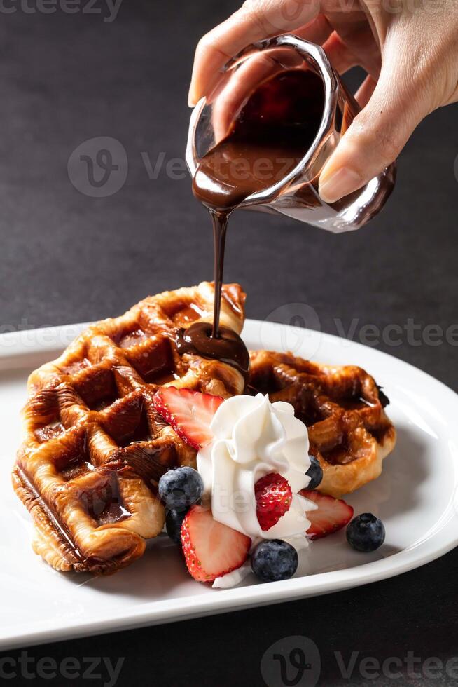CACAO Crispy Waffles with vanilla cream, strawberry, blueberry and hot melted chocolate served in dish isolated on dark background side view of baked cafe food photo