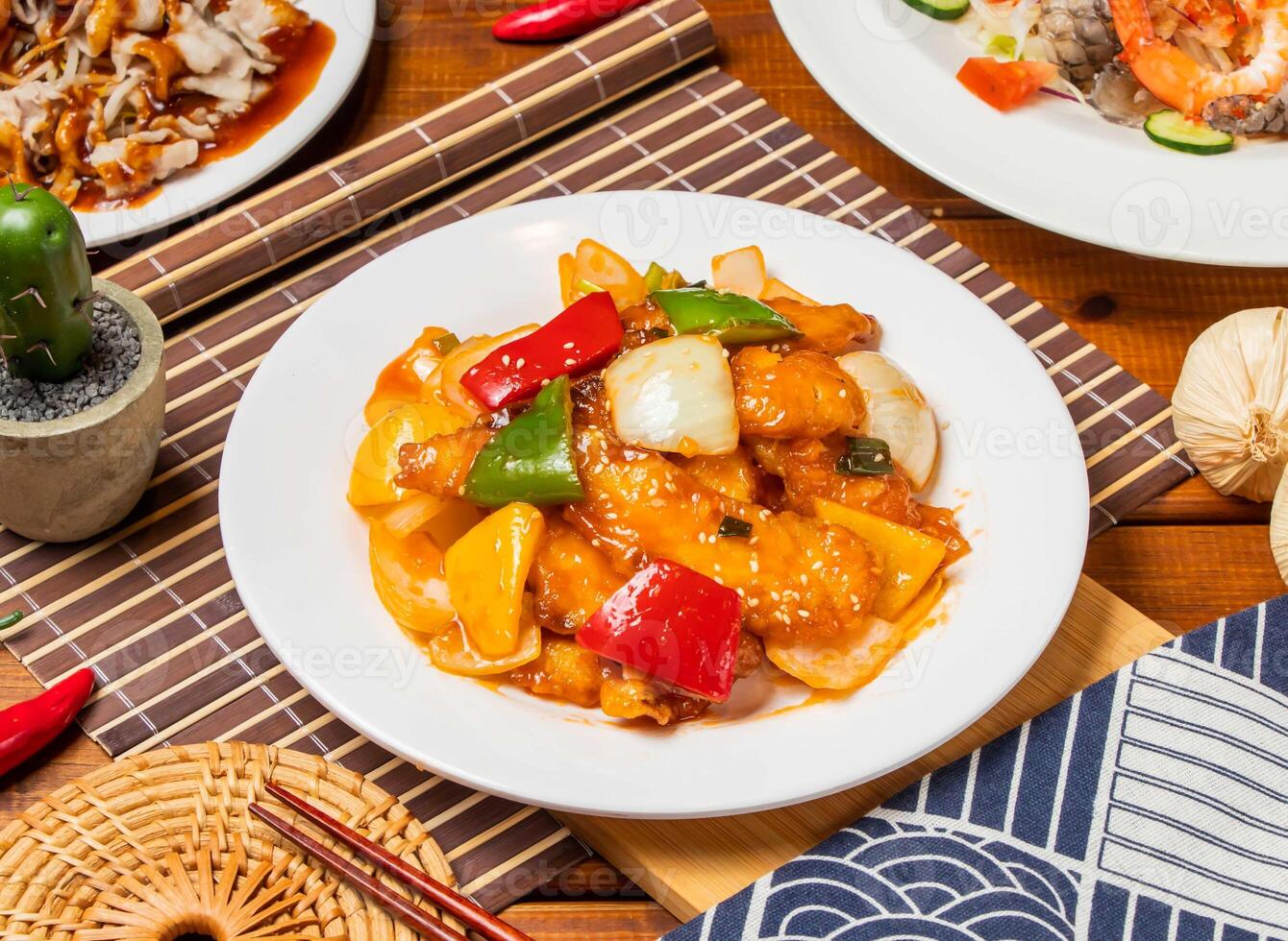 Sweet and sour fish fillet with red pepper, onion, tomato and chopsticks served in dish isolated on table side view taiwanese food photo