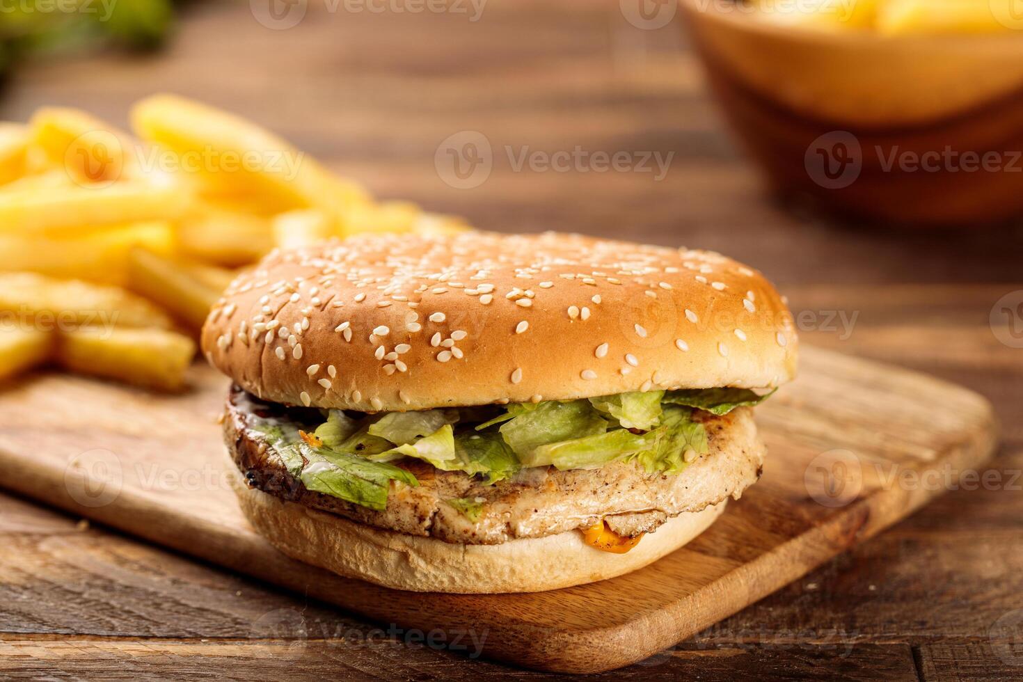 Chicken burger with french fries served in a cutting board isolated on wooden table background side view of fastfood photo