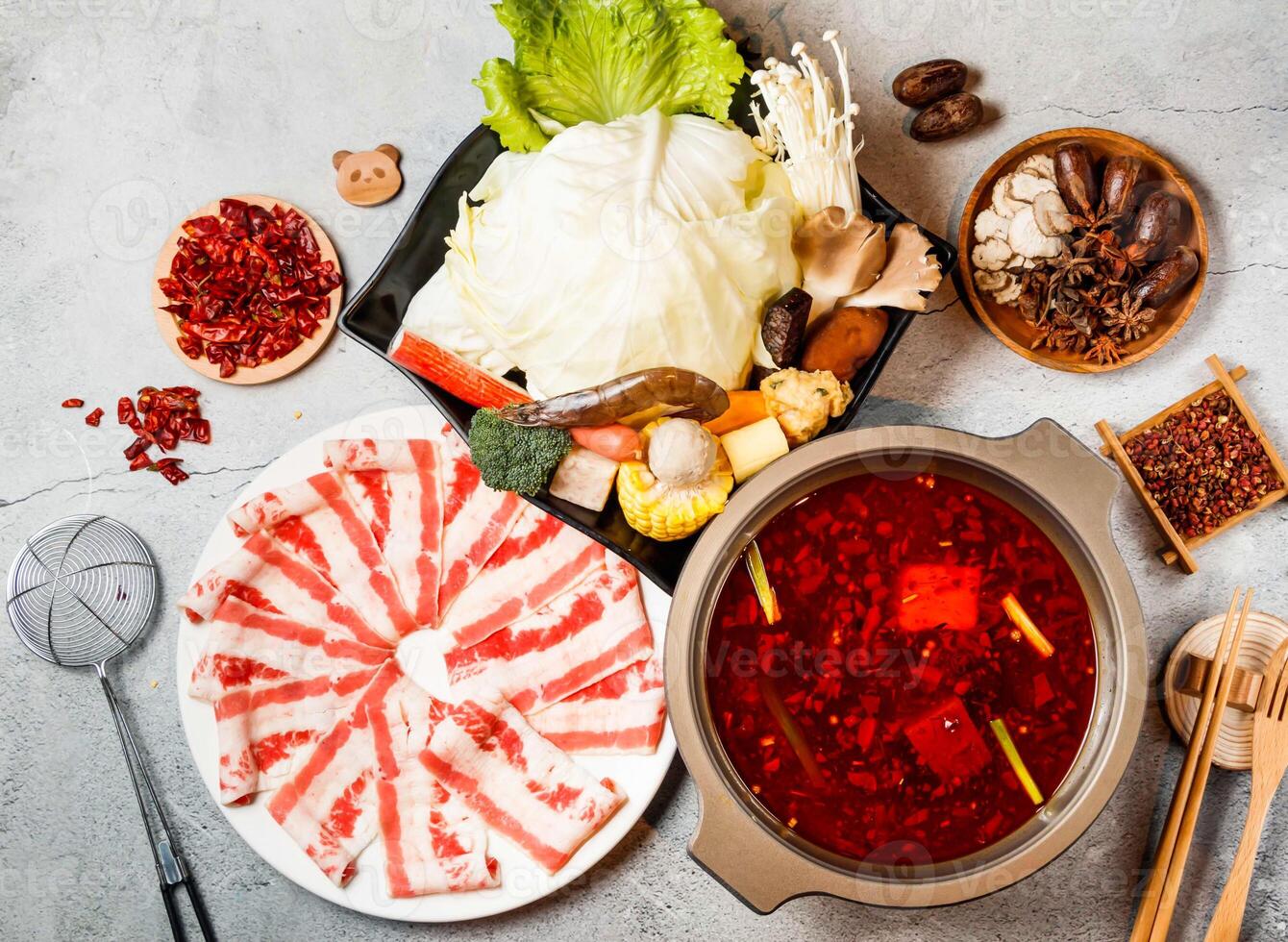 Spicy Hot Pot Set with meat slice, cabbage, baby corn, broccoli, mushroom, red chilli, chopsticks and fork served in pot isolated on background side view of taiwanese food photo