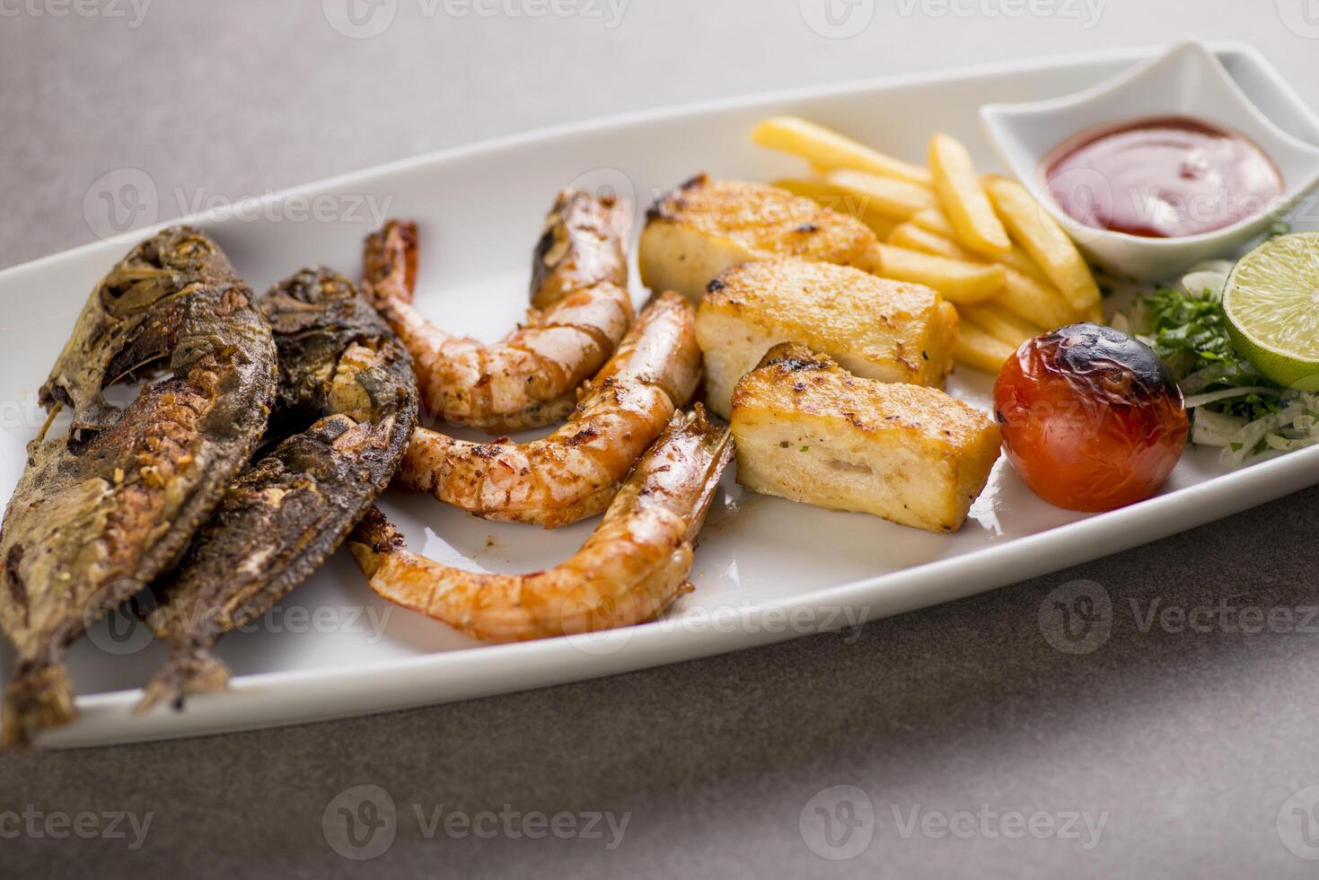 Seafood mix grill with fish tikka, shrimp, prawns, fries, and tomato sauce served in dish isolated on grey background top view of arabic food photo