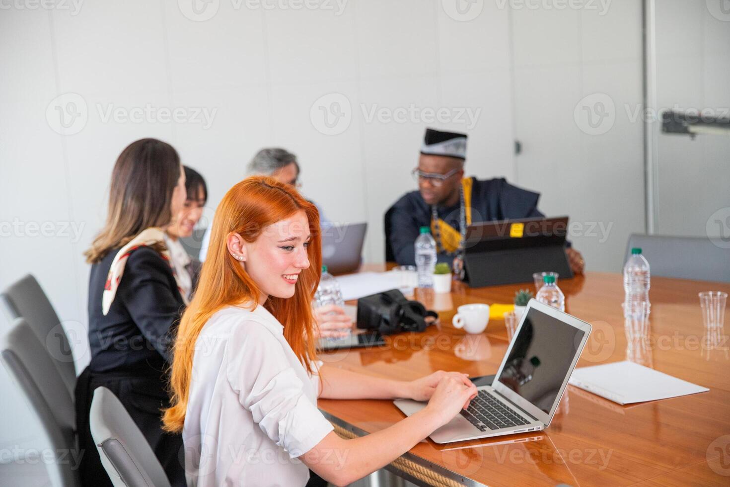 A businesswoman uses the laptop during a company meeting, her colleagues work in the background photo