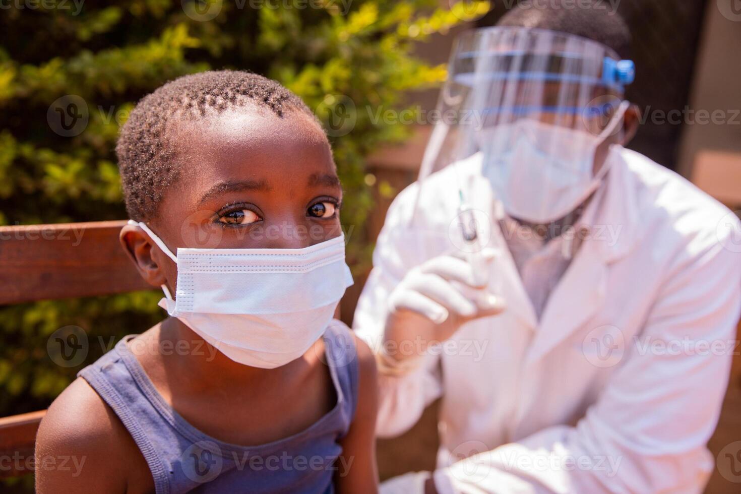 Portrait of a child in a clinic in Africa about to be vaccinated with the doctor beside him. photo