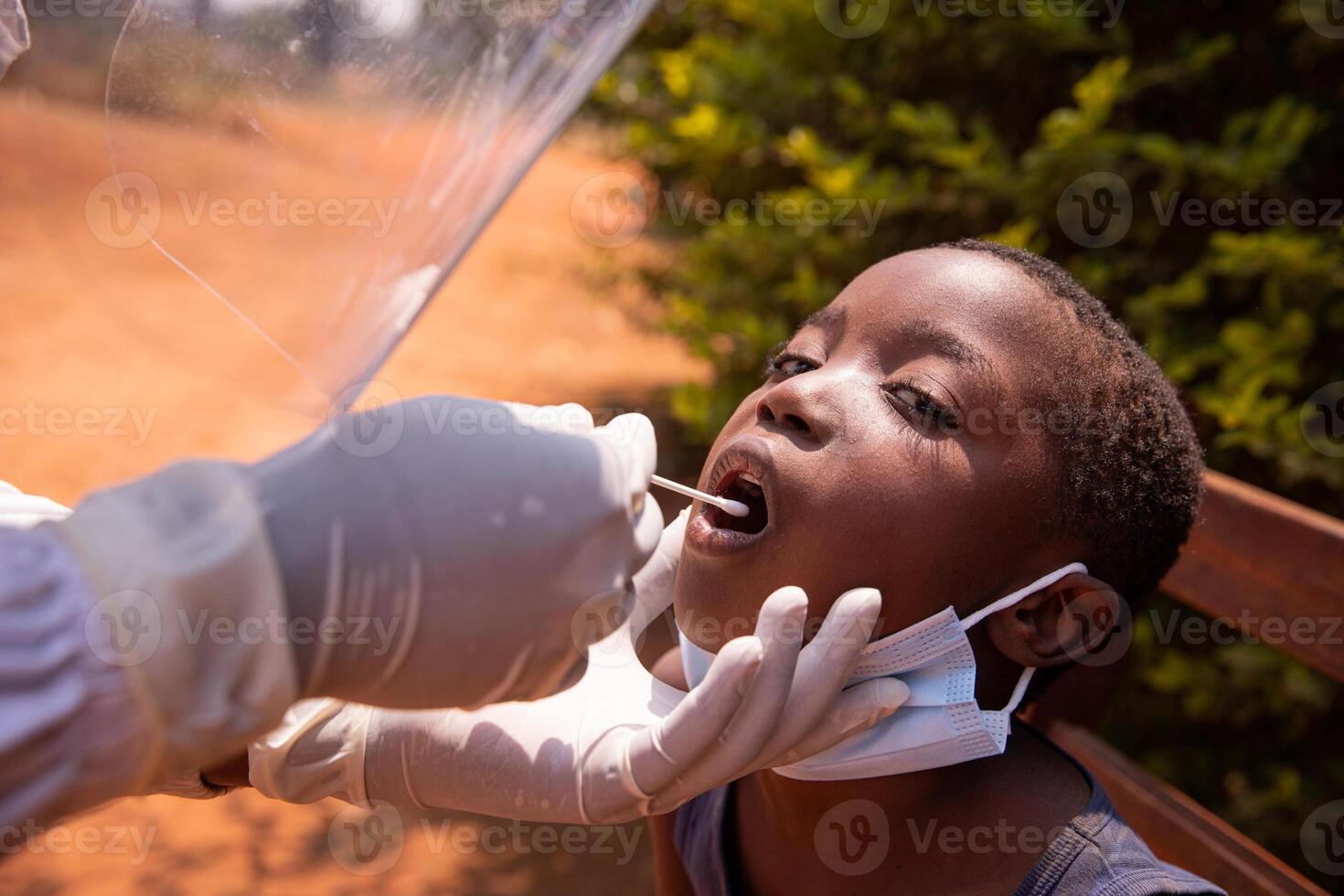 A doctor performs a coronavirus test on a child in Africa and inserts the swab down his throat photo