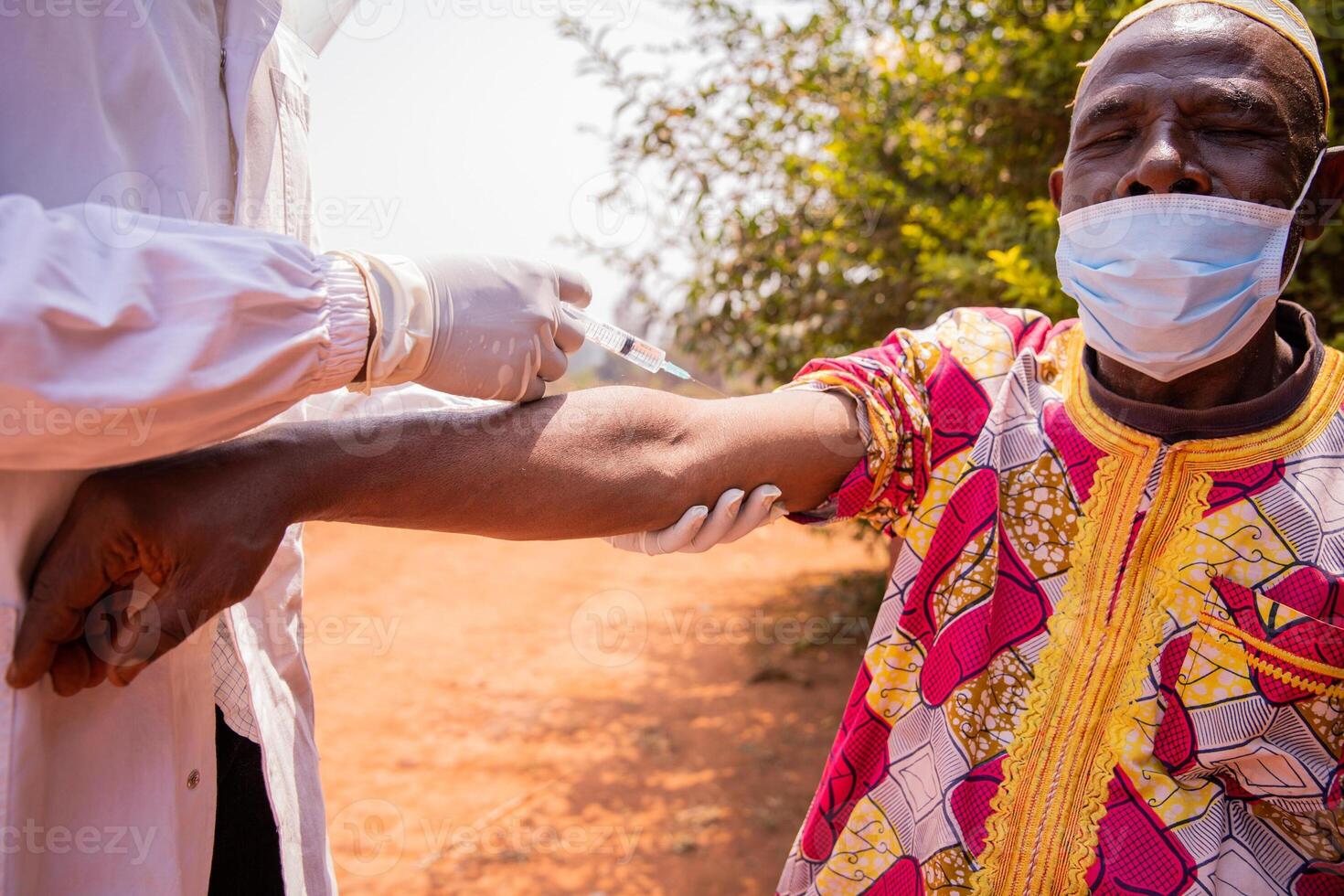 An African doctor vaccinates an elderly man with a syringe on his arm photo