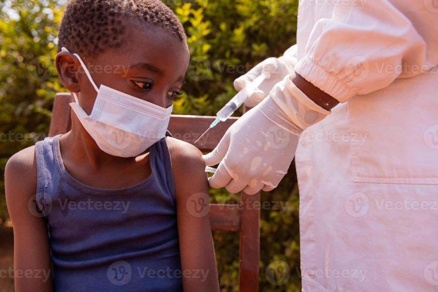 A little child wearing face mask sitting on a chair taking his injection photo
