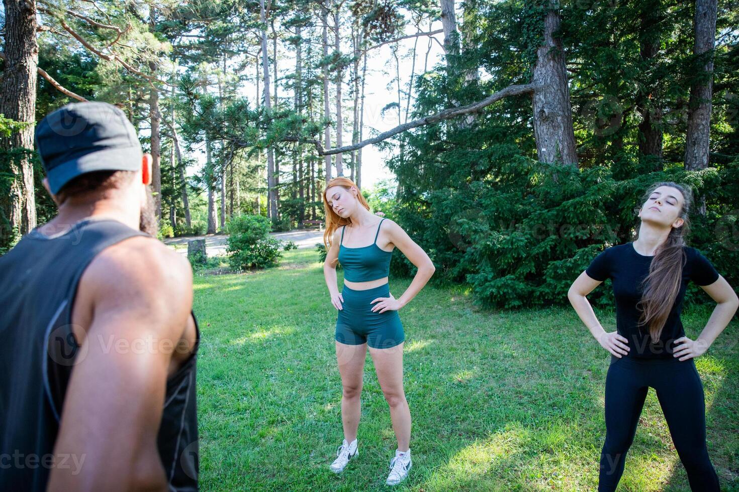 Three people are exercising in a park, personal trainer is holding a class with his athletes photo