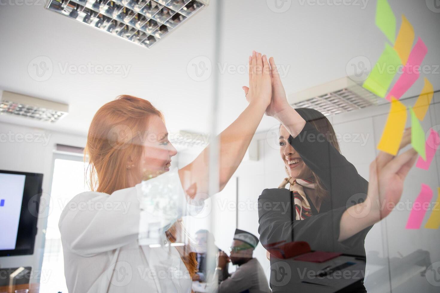 Two coworkers high-five each other during a meeting while writing on stick notes photo
