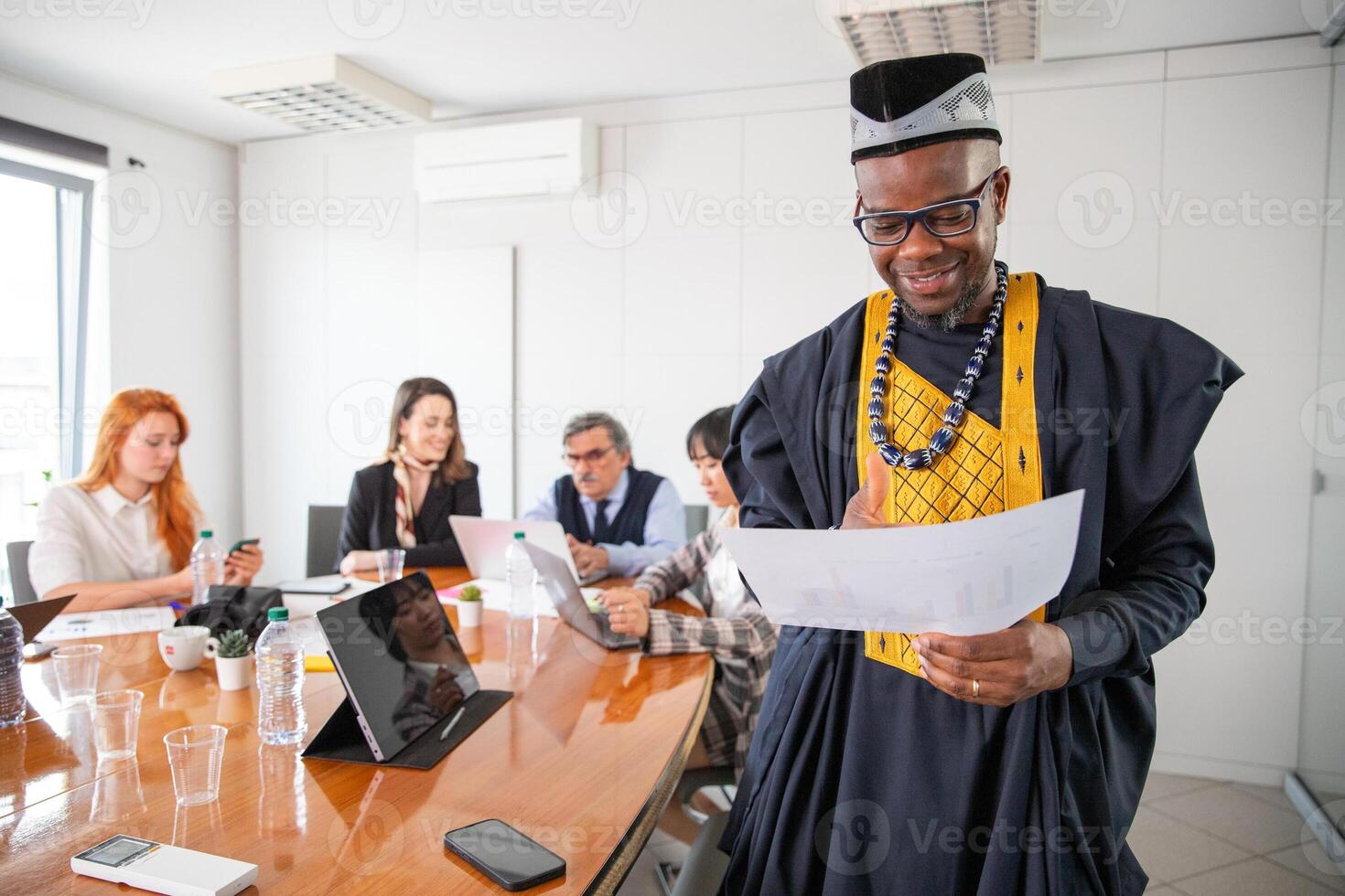 An African businessman analyzes charts during a meeting, his colleagues work in the background photo