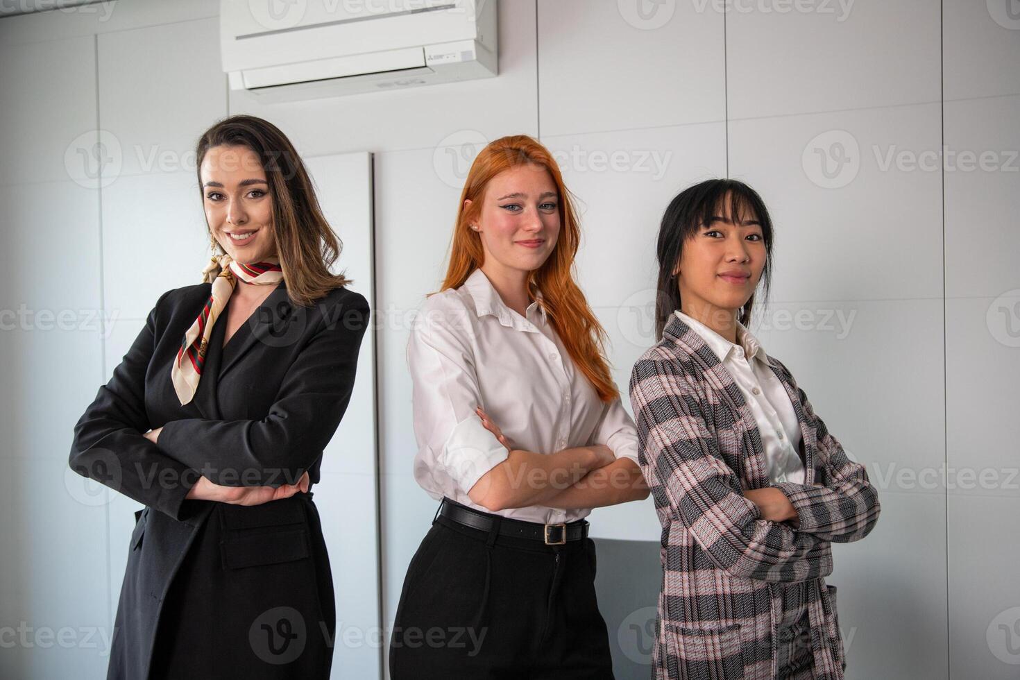 Three happy businesswomen with folded arms and confident expressions pose in the office photo