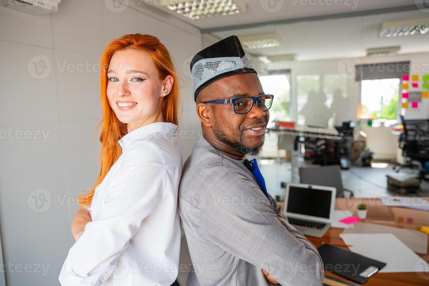 Two colleagues posing smiling in the office back to back, corporate life photo