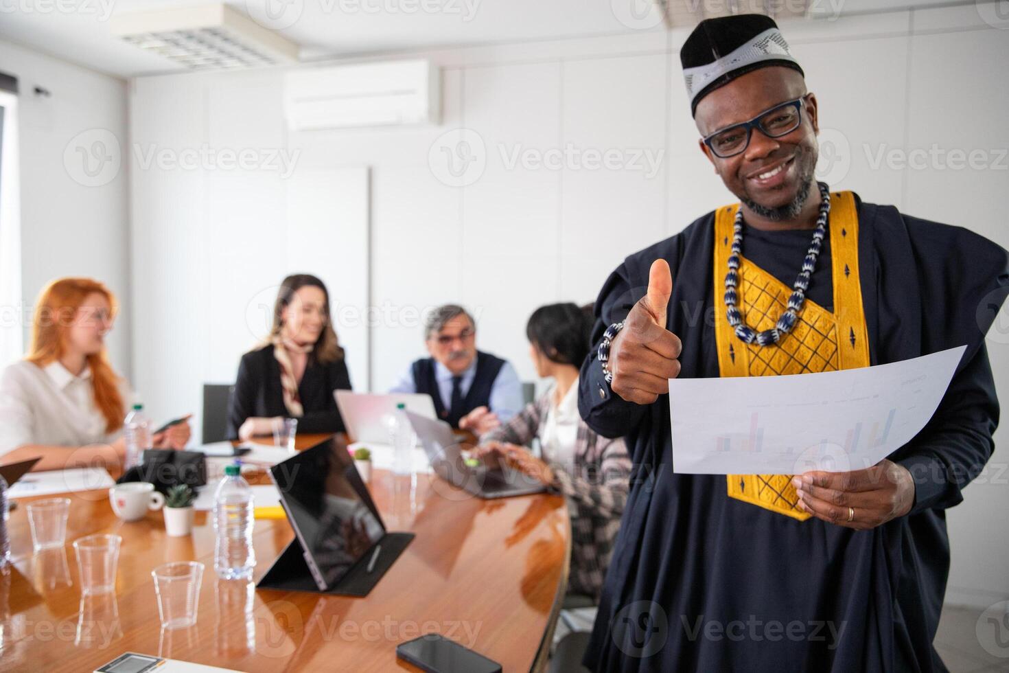 An African businessman during a meeting shows thumbs up, his colleagues work at the back photo