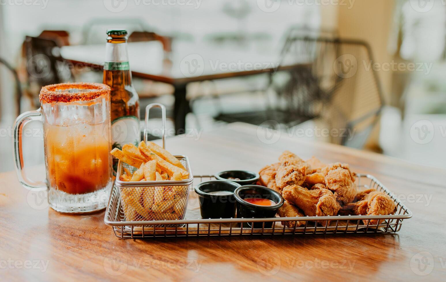 Delicious spicy chicken wings with fries and michelada accompanied by beer served on a restaurant table photo