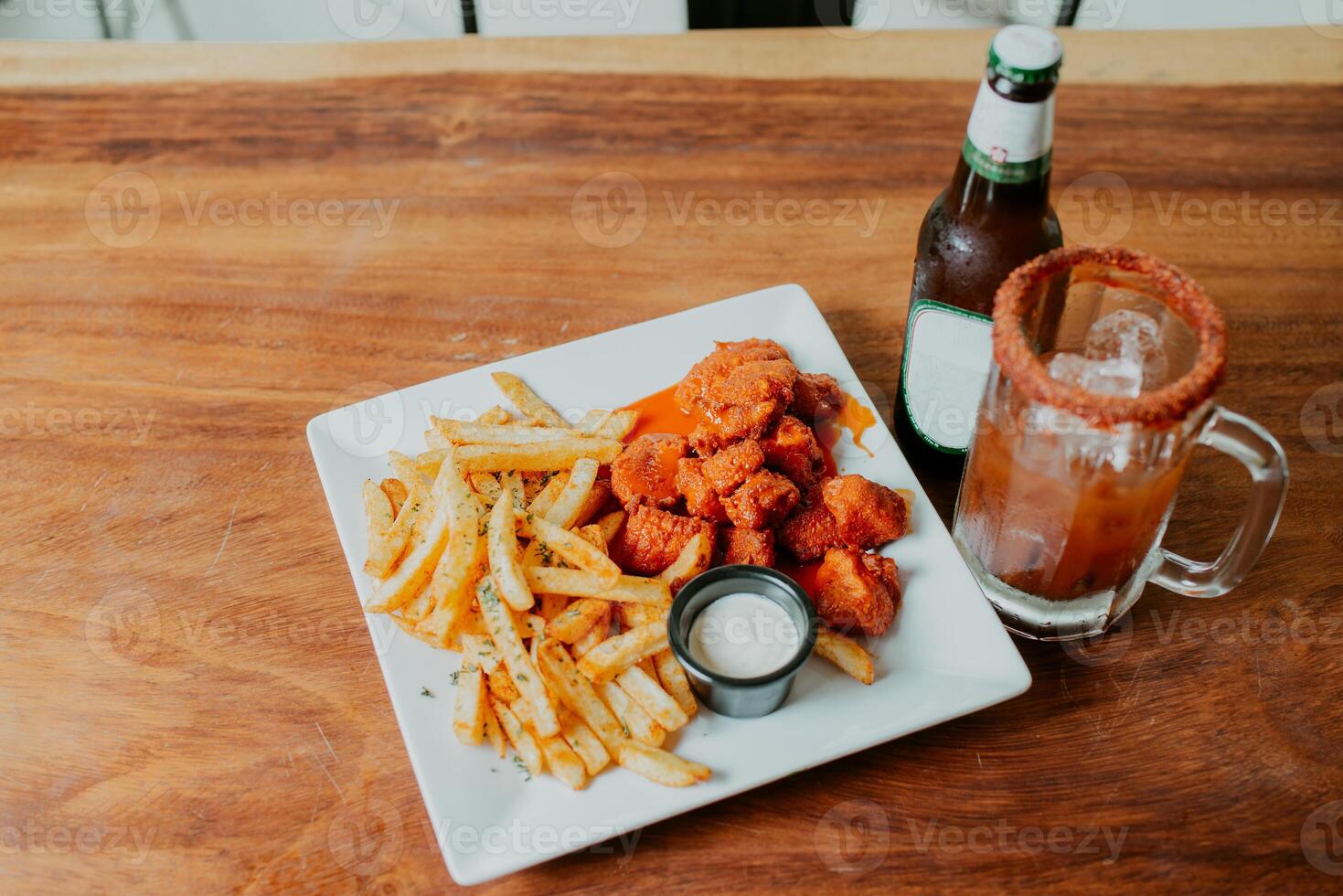 Traditional spicy wings with fries and michelada drink accompanied with beer served on wooden table photo