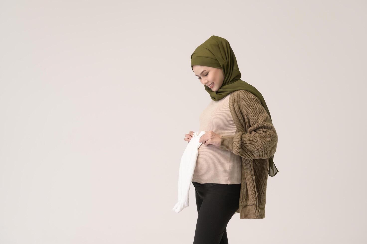 Portrait of Pregnant muslim woman in hijab holding baby cloth over white background studio photo
