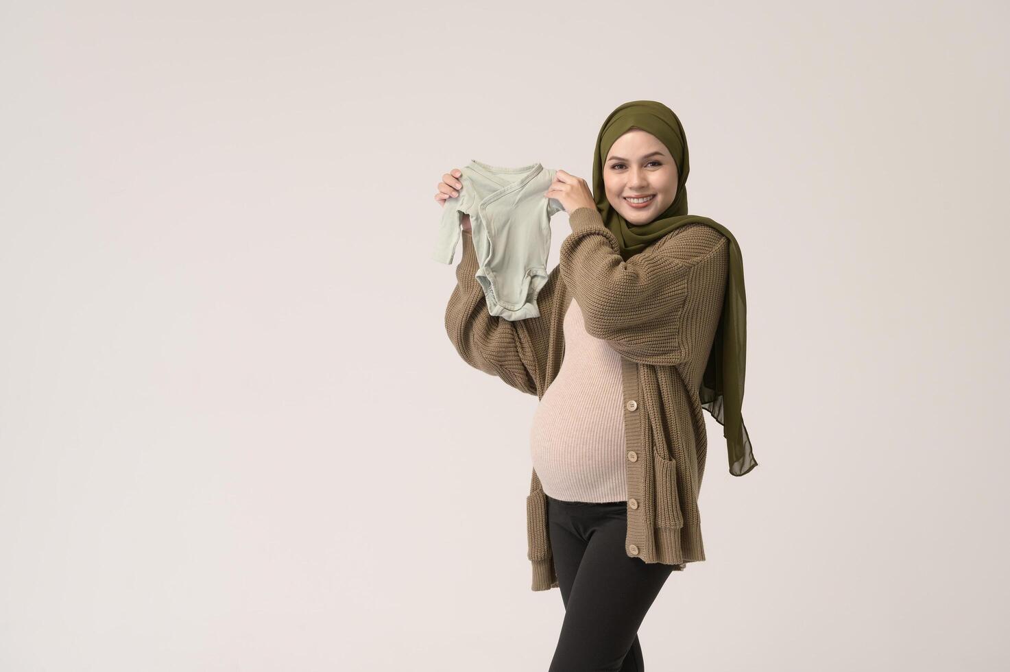Portrait of Pregnant muslim woman in hijab holding baby cloth over white background studio photo