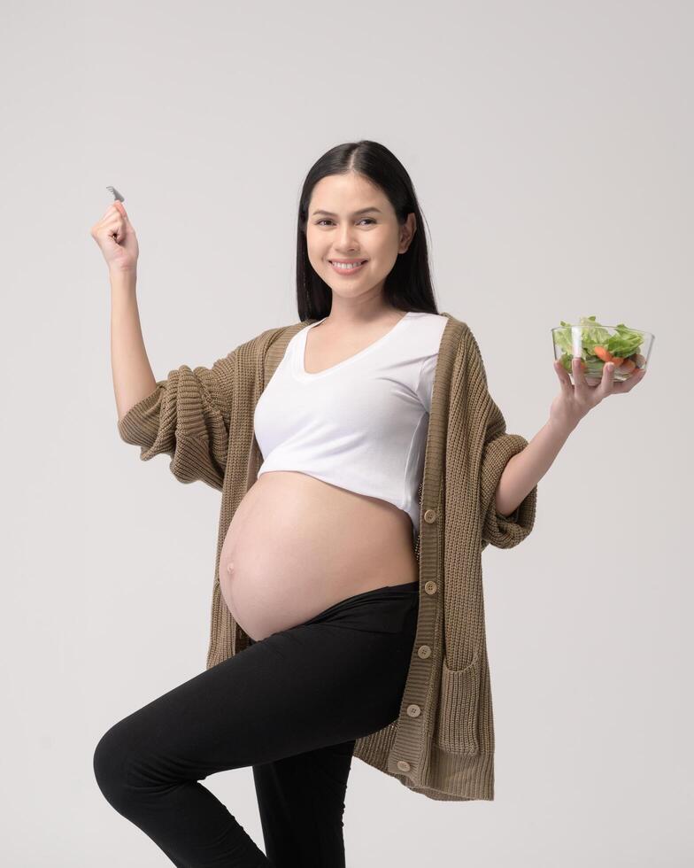 retrato de hermosa embarazada mujer comiendo ensalada terminado blanco antecedentes estudio, salud y maternidad concepto foto