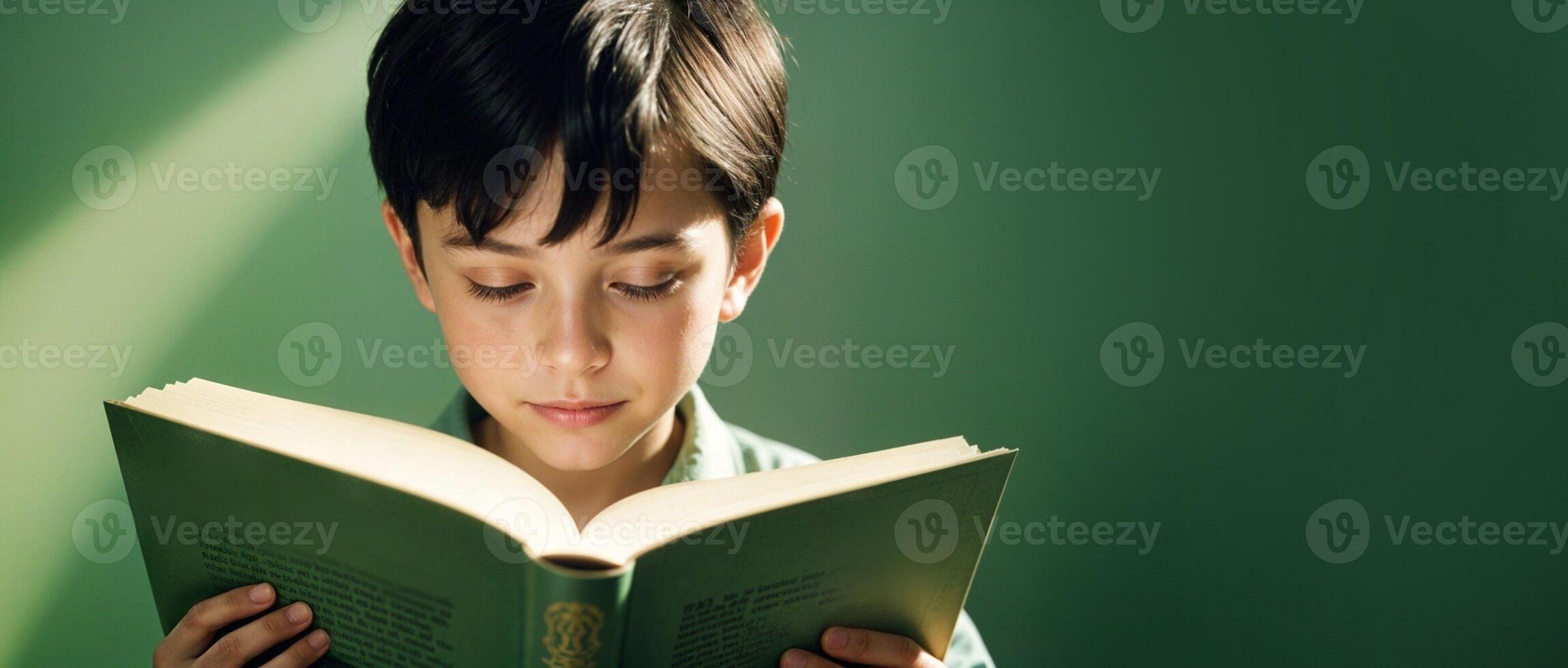 Isolated Portrait of 10-year-old Caucasian boy with dark hair attentively reads a book on a green copy space background. design for banners, website, promotional materials. High quality photo. photo