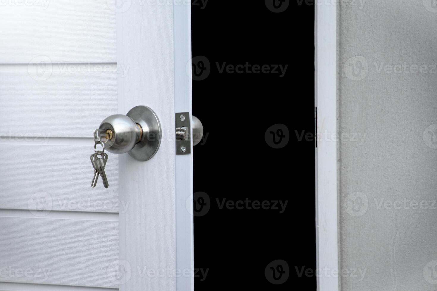 Open white door and silver knob with keys against gray concrete isolated on black background for concept of open the door or close the door and forget the key. photo