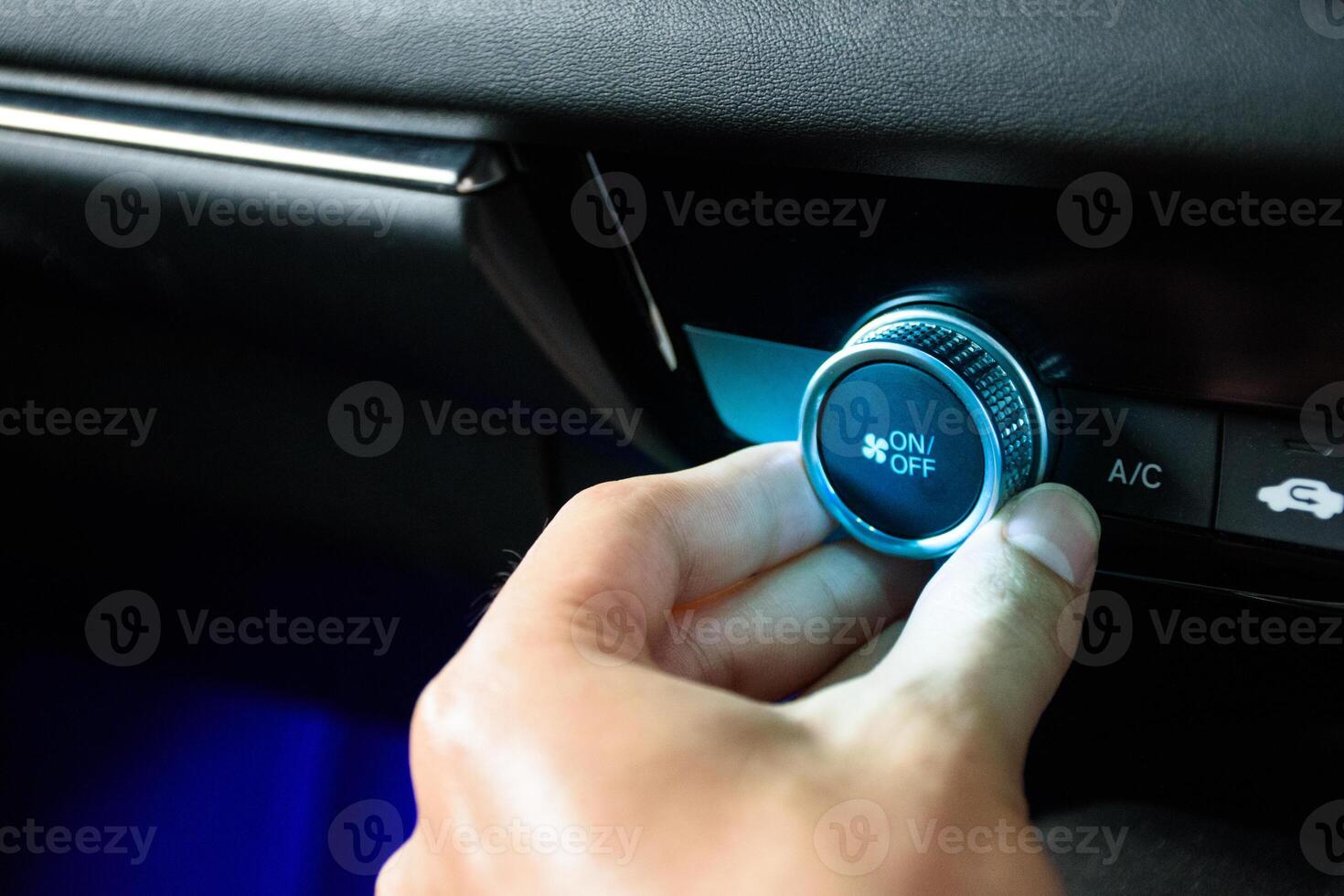 Hand turning the button car air conditioning fan to air condition the interior of a modern luxurious car with blue light in 2024. photo