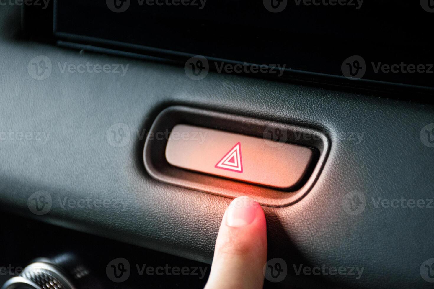 Finger pressing the emergency light button on a car to symbolize a car accident along with a red light on the control panel button. photo