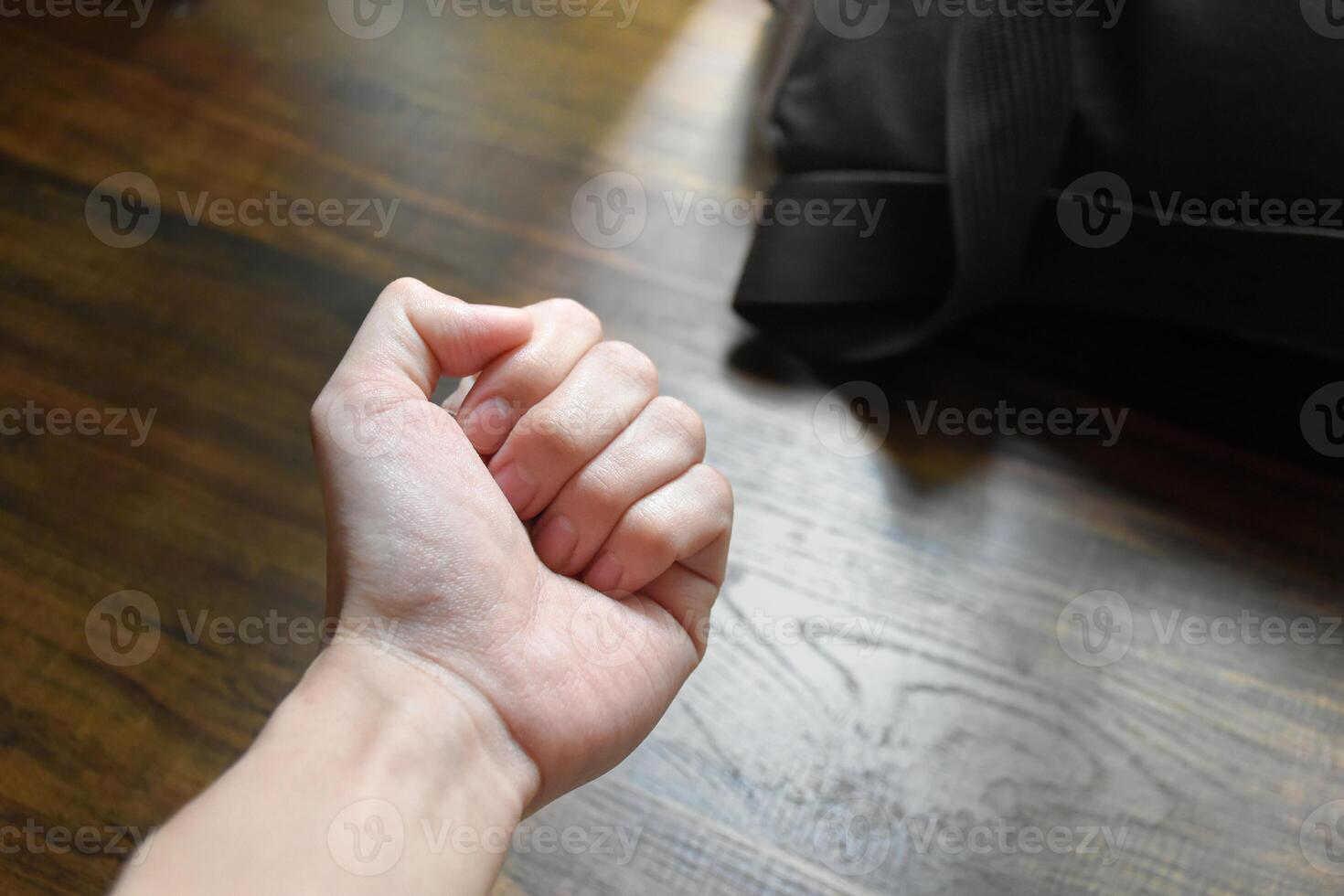 Fist of hand on desk soft sunlight and work bag background,hands on the table, hands conveying anger,hands showing determination,pressure at work,wood pattern work table,black work bag. photo