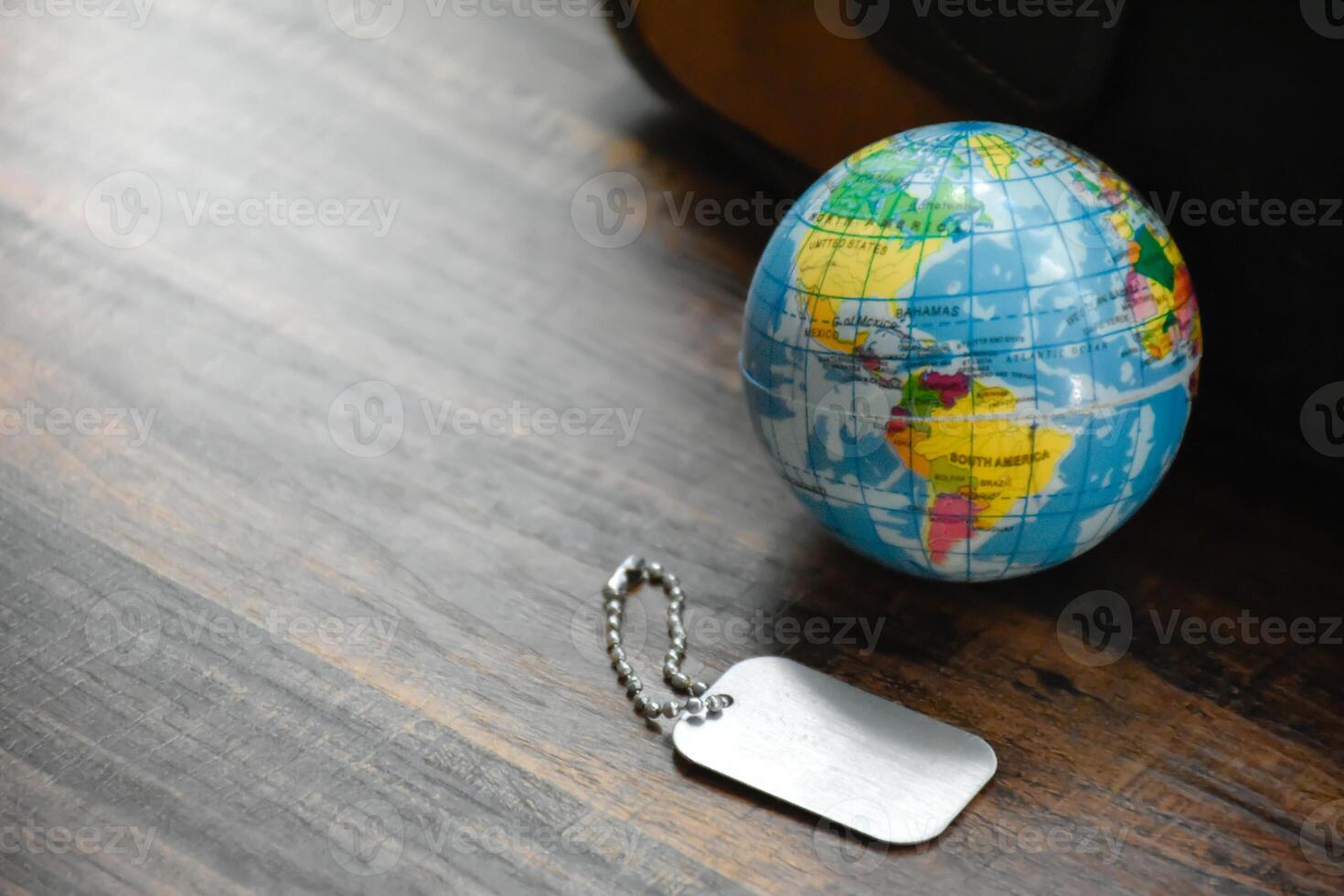 Earth Globe and Dog Tag on wood pattern work desk and soft sunlight background,Dog Tag empty,World and map of Americas,Top view with copy space,Desktop equipment,Concept of Travel and Work,Earth map. photo