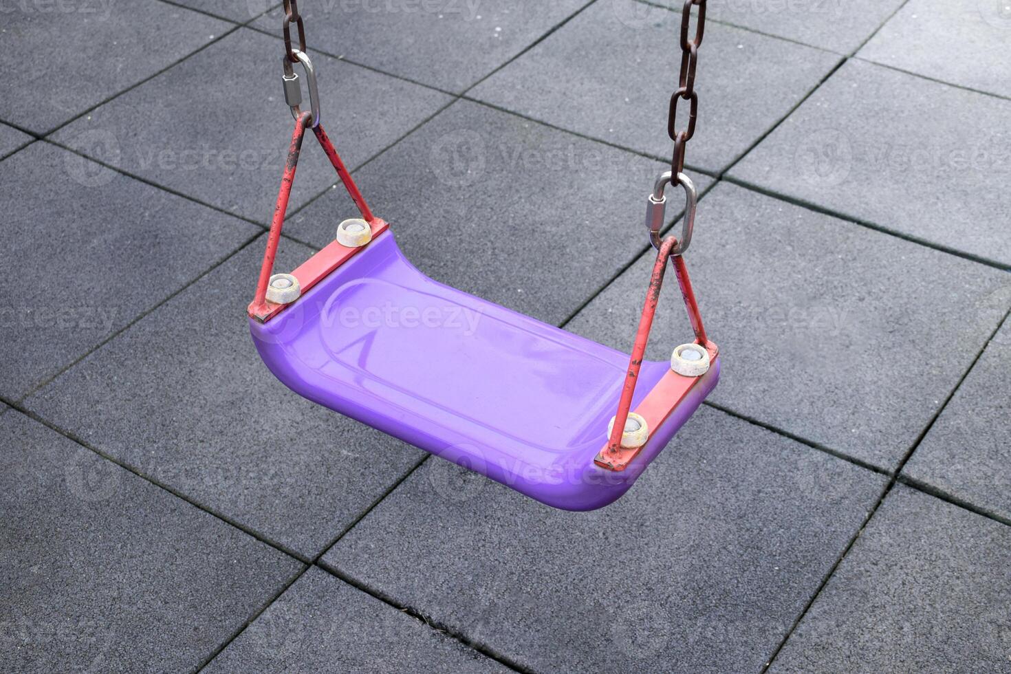 Swing purple on playground black rubber floor background, Alone swing for children on black rubber floor, Swing purple seat, concept of playing and children on soft sunlight, isolated background. photo