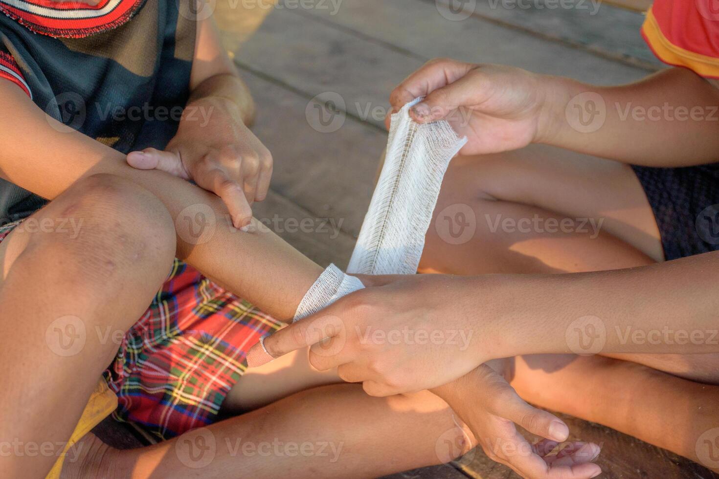 Two boys are helping to bandage a wound on their arm with gauze bandage from a childhood accident for first aid and medical concepts. Two men are giving first aid by bandaging a wound. photo