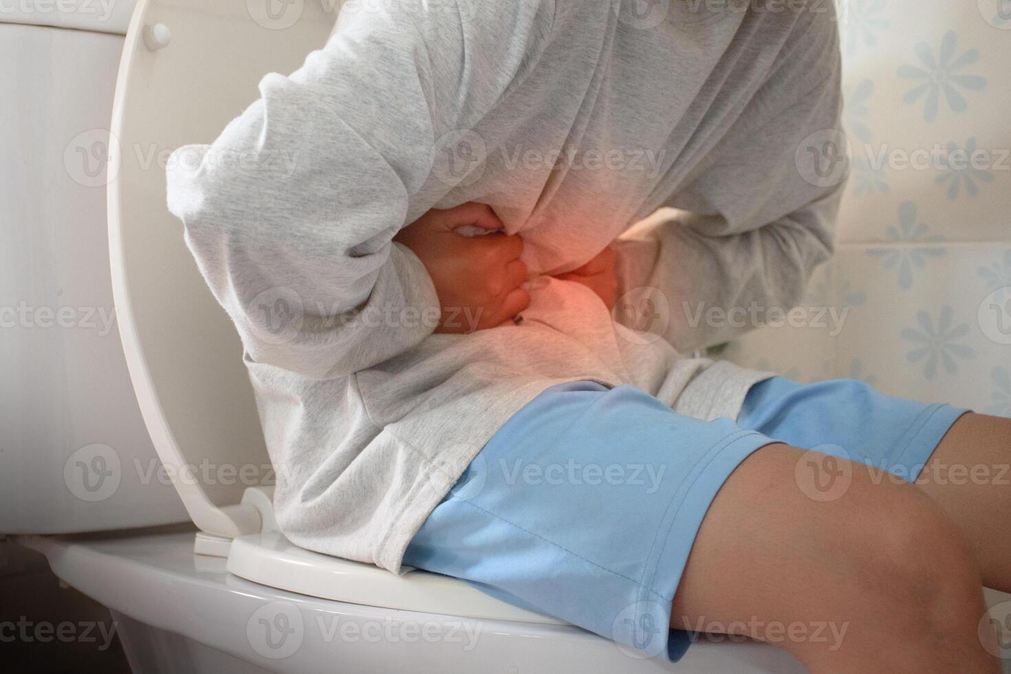 Man sitting on toilet and holding his stomach with stomach pain causes of gastritis or constipation with red dot in bathroom and sunlight blurred background concept of medical and health problems. photo