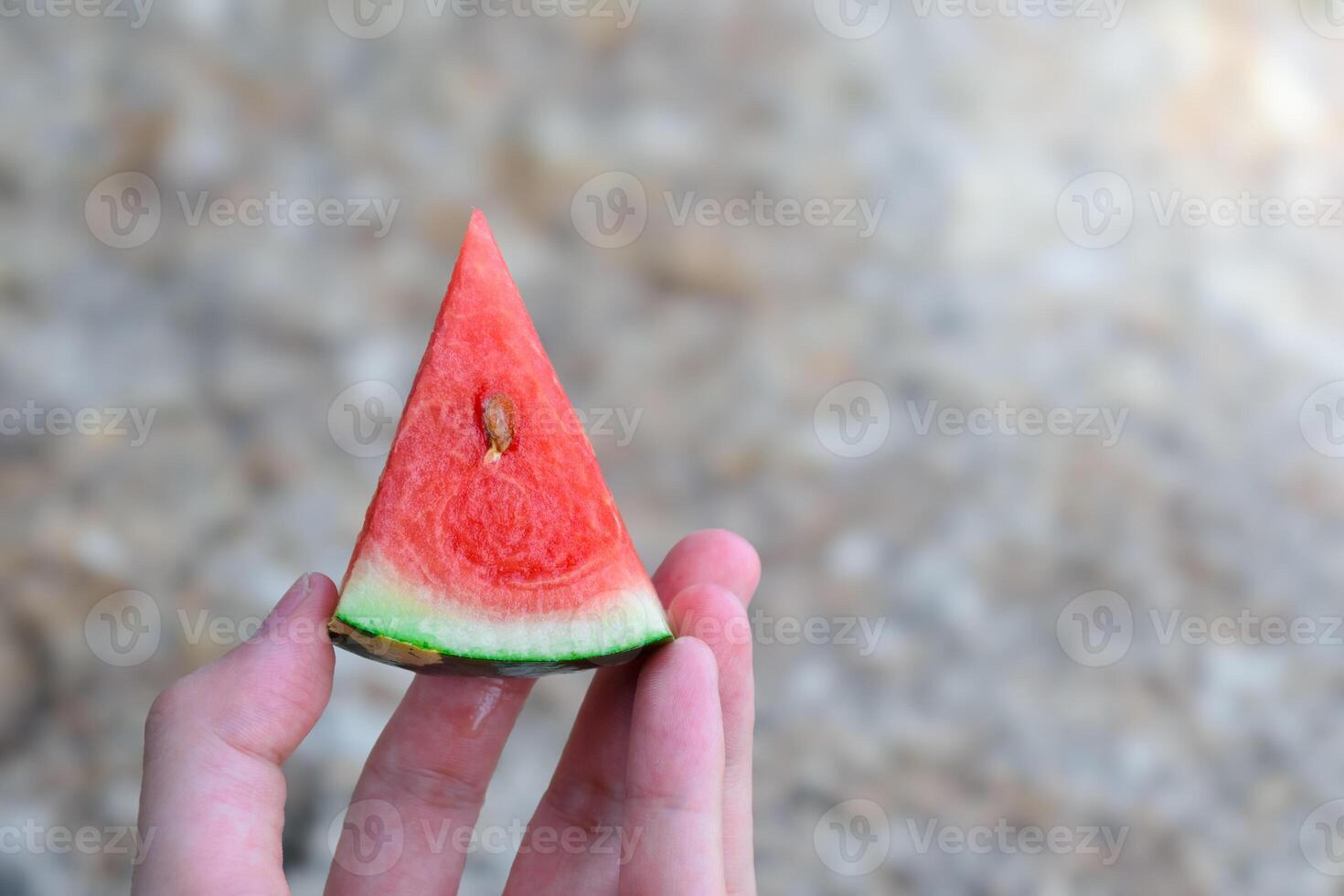 Hand holding watermelon cut into triangular pieces close-up in stone pattern floor and sunlight blurred background for design and health fruit concept. photo